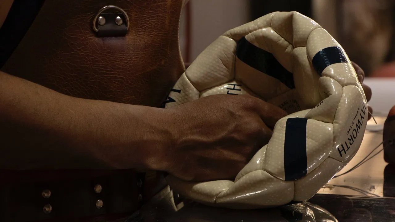 A ballmaker in the Monguí workshop holding an unfinished Hayworth Athletic ball mid-stitch.